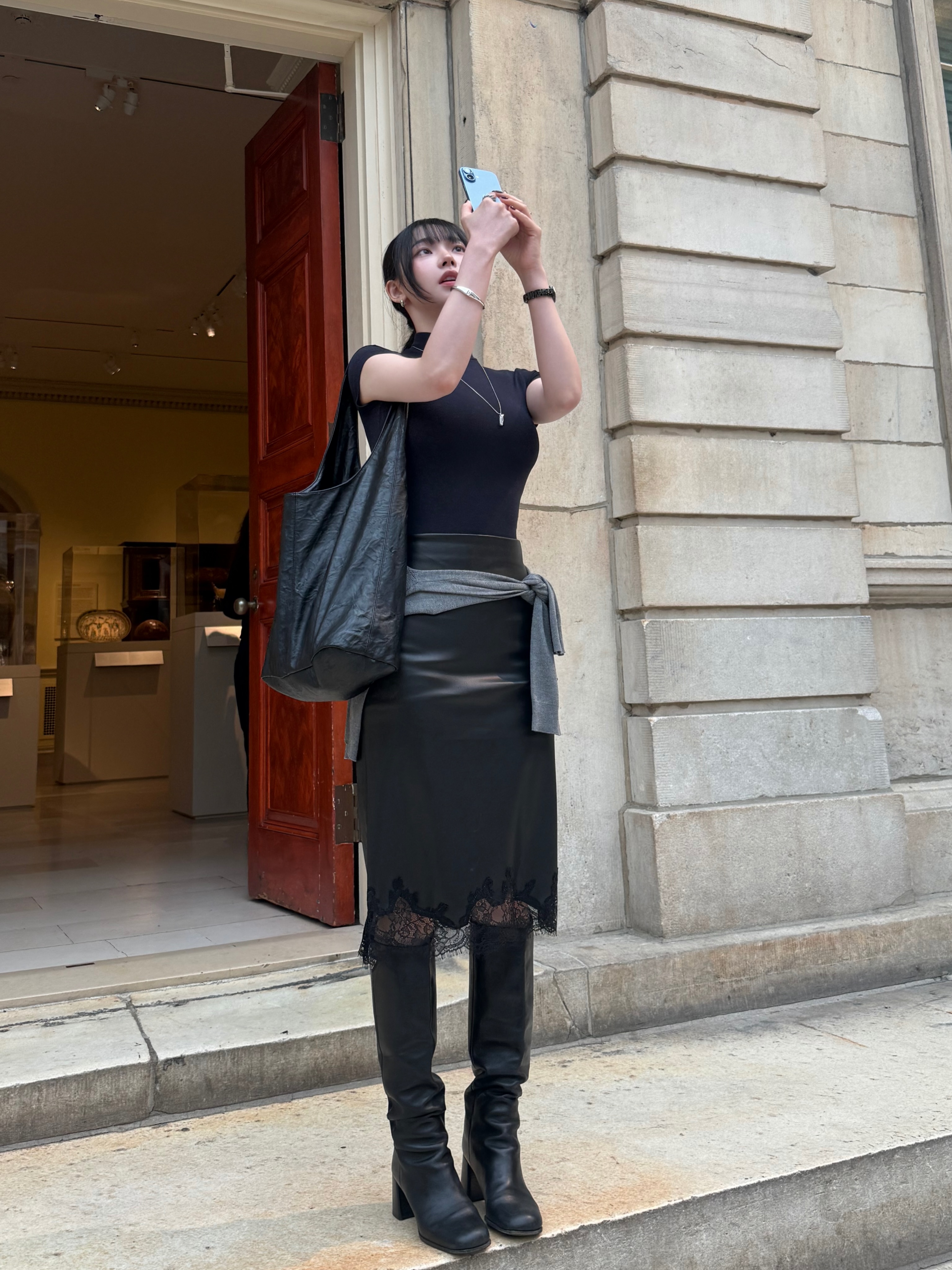 美術館の前でスマートフォンを構える、黒のTシャツ姿のaespa・カリナさん