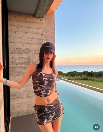 沖縄の海とプールを背景に、迷彩のキャミソールとミニスカートを着た重盛さと美さん