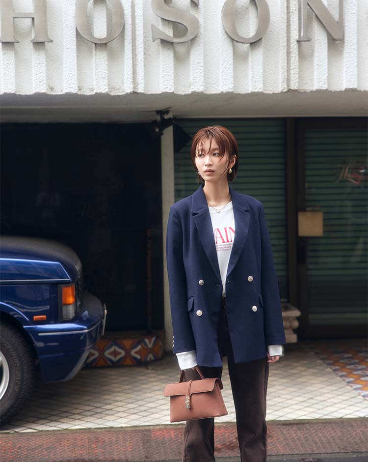 VISの公式撮影で、金属ボタンが4つあるネイビーのジャケット、白いTシャツと黒いパンツを着る岡崎紗絵さん