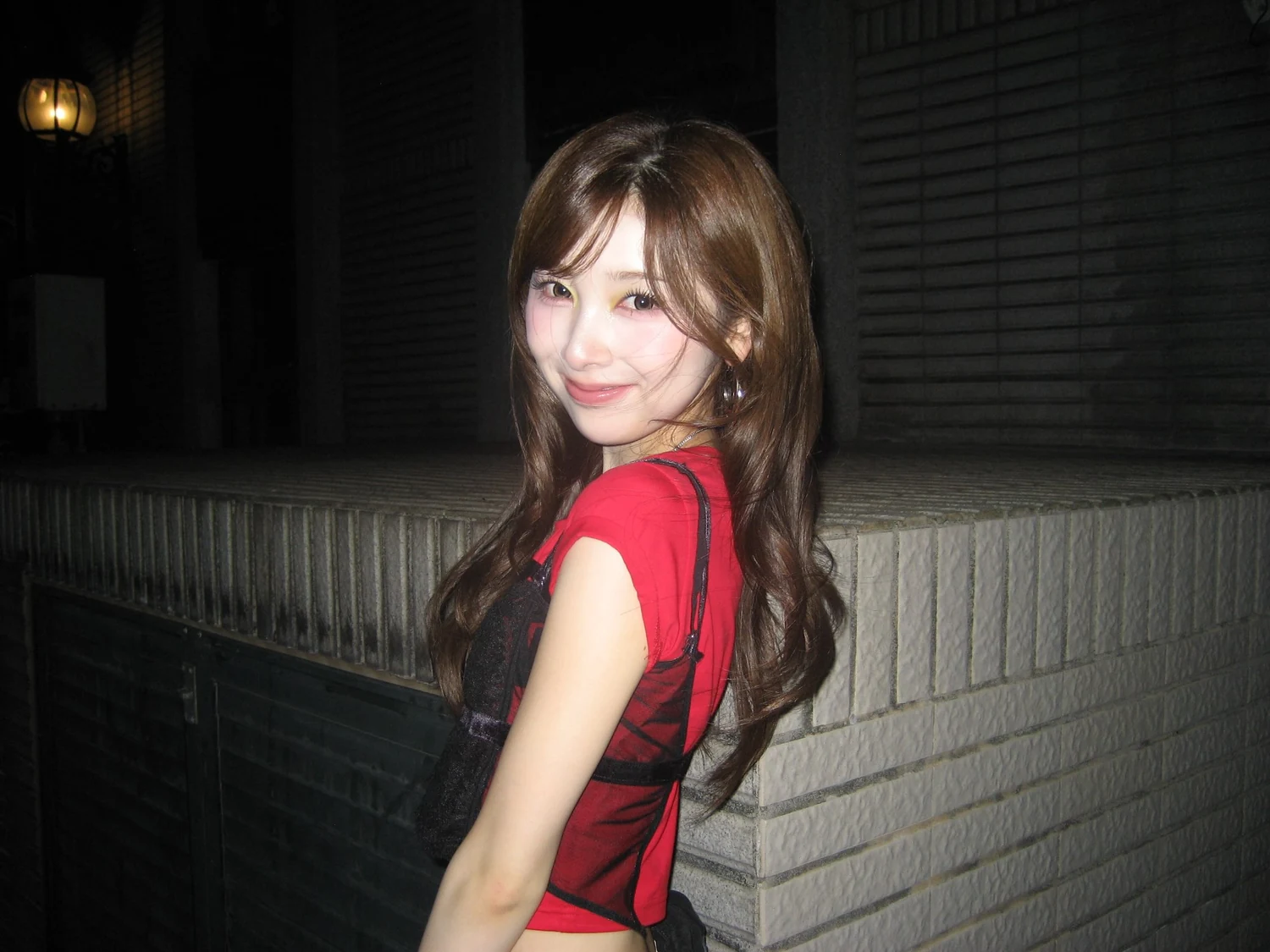 街なかで振り向いて笑うNiziUのMIIHIさん。赤いトップスに黒いビスチェを重ねている