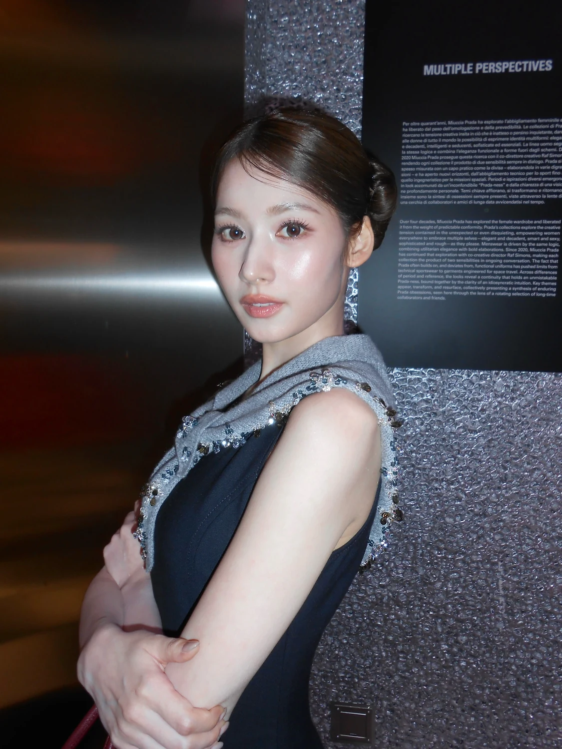 グレーの飾り付きスカーフとネイビーのドレスを着て腕を組むSANAさん